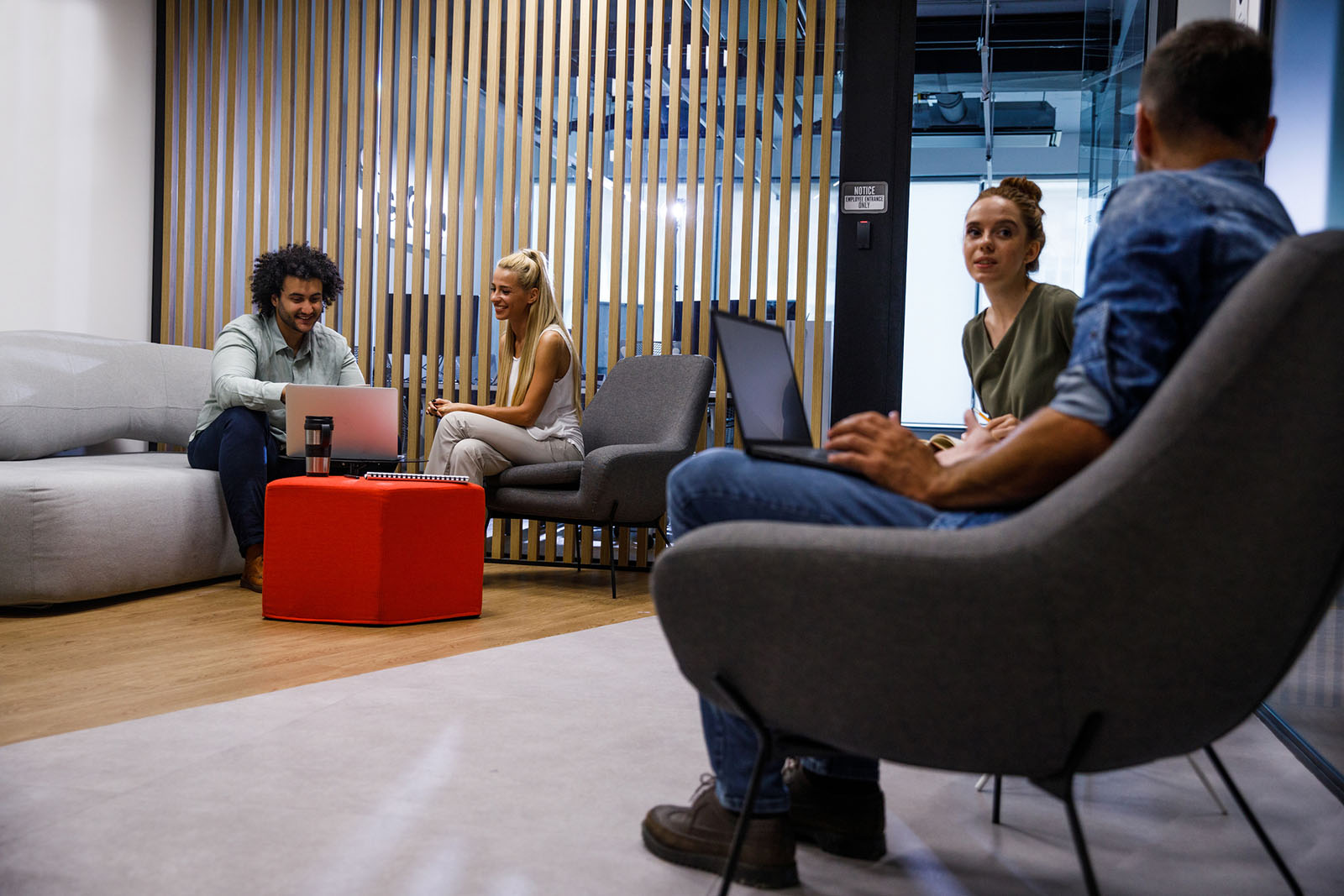 People sitting on sofas with laptops and talking in a modern office lounge area.