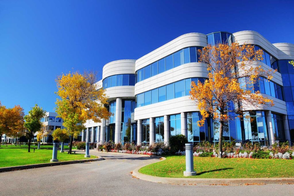 Modern office building with glass windows, surrounded by trees with autumn foliage under a clear blue sky.