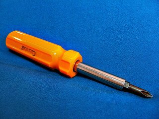 Orange-handled screwdriver with a Phillips head, resting on a blue surface.